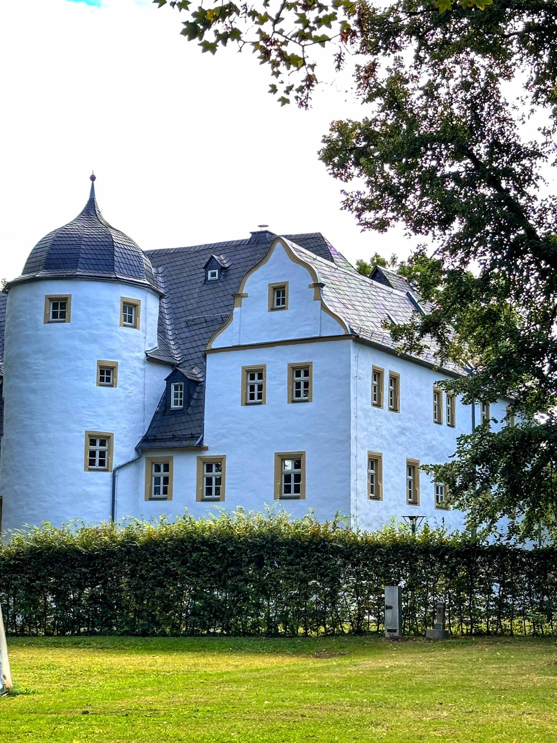 Der Rundturm des Schlosses Eyba hinter alten Bäumen